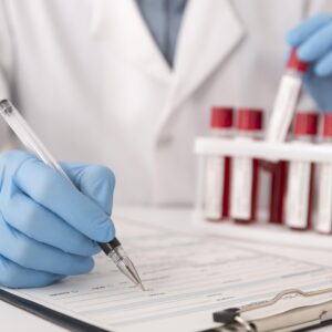 Picture of a person in a lab coat writing on a clipboard with blood vials in the background
